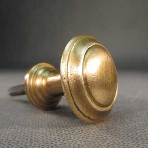 Może przedstawiać: Mosiężny gałka z zaokrąglonym wierzchołkiem i żebrowaną podstawą. Gałka ma błyszczące wykończenie i lekko postarzony wygląd.