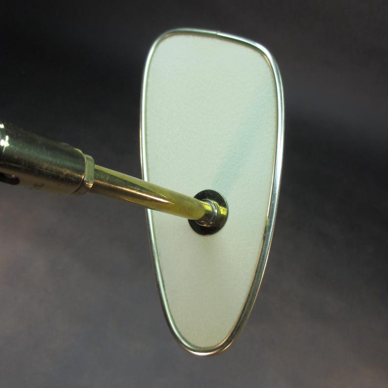 Pu&ograve; includere: Uno specchio retrovisore vintage in ottone e cromo con una superficie riflettente ovale bianca. Lo specchio &egrave; attaccato a un braccio lungo e sottile in ottone.