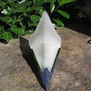 May include: A wall sconce light fixture featuring a frosted glass shade with a geometric pattern and a polished chrome metal base. The shade is shaped like a tall, pointed leaf or sail, with vertical and angular lines etched into the glass surface.