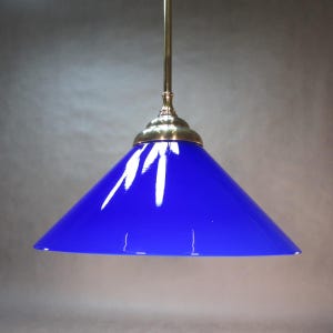 Peut inclure: Un luminaire suspendu avec un abat-jour en verre bleu vif. L'abat-jour est en forme de cône et est suspendu à un raccord en métal de couleur laiton. Ce luminaire est un design classique, adapté à divers styles d'intérieur.