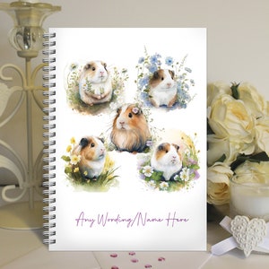 May include: A white spiral bound notebook featuring a watercolour illustration of four guinea pigs in a field of flowers. The text "Any Wording/Name Here" is printed in purple at the bottom of the notebook.