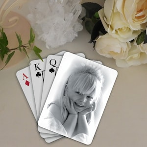 May include: Four playing cards, the Ace of Diamonds, King of Clubs, Queen of Spades, and a blank card with a black and white photo of a young girl smiling.