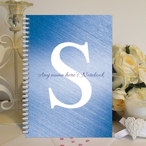 May include: A blue spiral notebook with a white letter "S" and the text "Any name here's Notebook" in blue.