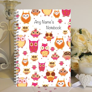 May include: A white spiral notebook with a colourful owl pattern. The cover features pink, orange and brown owls with various designs. The text "Any Name's Notebook" is printed in black on the cover.