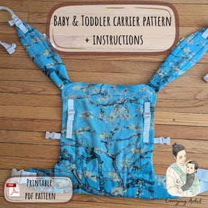 Op de afbeelding: Een baby- en peuter draagzak patroon met instructies. De draagzak heeft een blauwe stof met een boomtak ontwerp en witte bandjes en gespen. De tekst "Baby & Toddler Carrier Pattern + Instructions" wordt weergegeven. "Printable PDF Pattern" is ook zichtbaar.
