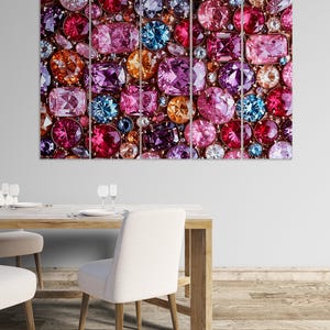May include: A multi-panel artwork featuring a mosaic of colorful gemstones. The gems are in various shapes and sizes, with shades of pink, purple, orange, and blue. The artwork is displayed above a wooden dining table with white chairs.