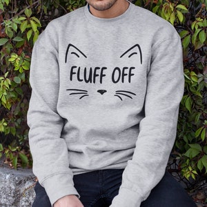 May include: A grey sweatshirt with a black cat face graphic and the text "FLUFF OFF" printed on the front.