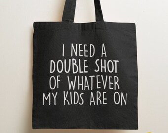 May include: A black tote bag with two shoulder straps featuring the white printed text I NEED A DOUBLE SHOT OF WHATEVER MY KIDS ARE ON. The bag is constructed from a solid black fabric and displays the text in a clean, sans-serif white font.
