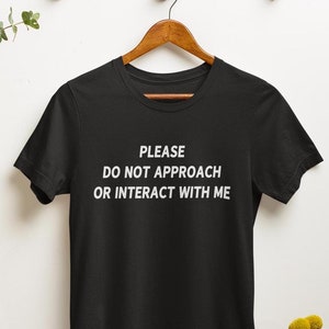 K&ouml;nnte beinhalten: Schwarzes T-Shirt mit wei&szlig;em Text, der "PLEASE DO NOT APPROACH OR INTERACT WITH ME" lautet.