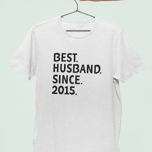 Op de afbeelding: Wit T-shirt met zwarte tekst die "BEST. HUSBAND. SINCE. 2015." luidt.