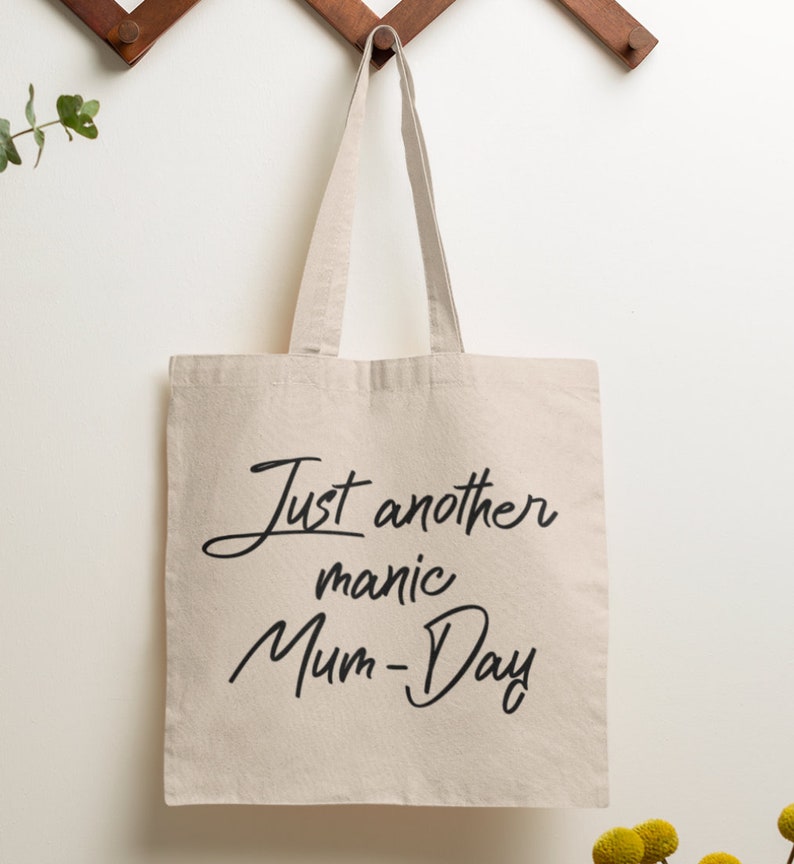 May include: A beige canvas tote bag with black text that reads "Just another manic Mum-Day".