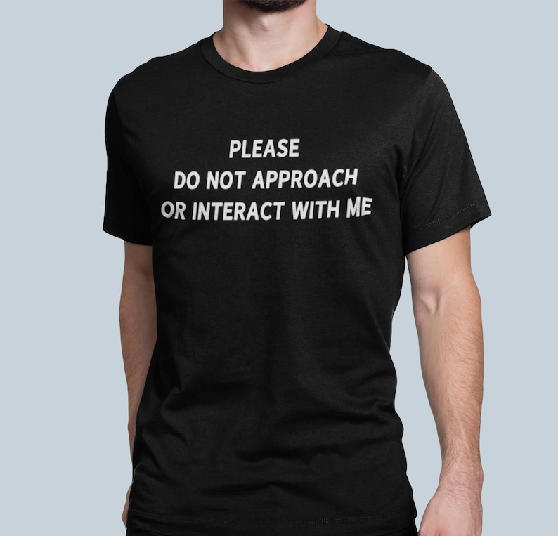 K&ouml;nnte beinhalten: Ein schwarzes T-Shirt mit dem Text "PLEASE DO NOT APPROACH OR INTERACT WITH ME" in wei&szlig; gedruckt.