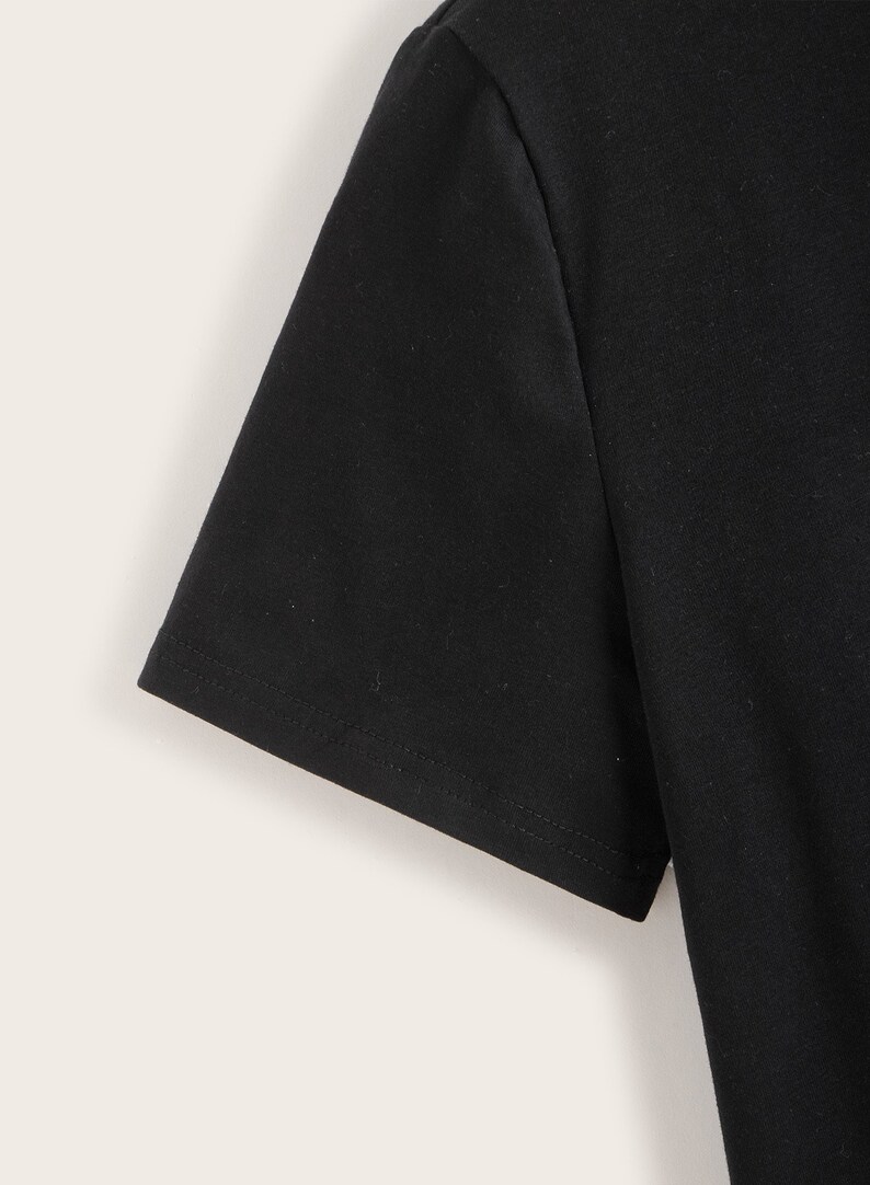 K&ouml;nnte beinhalten: Nahaufnahme des schwarzen Kurzarm-&Auml;rmels eines T-Shirts. Der &Auml;rmel hat einen gen&auml;hten Saum.