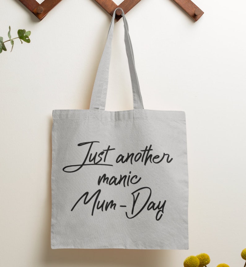 May include: A white canvas tote bag with black text that reads "Just another manic Mum-Day".