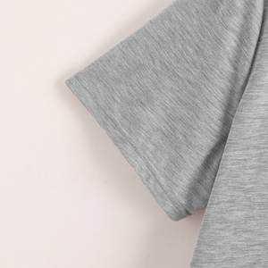 K&ouml;nnte beinhalten: Nahaufnahme des &Auml;rmels eines grauen T-Shirts. Der Stoff hat eine subtile Textur.