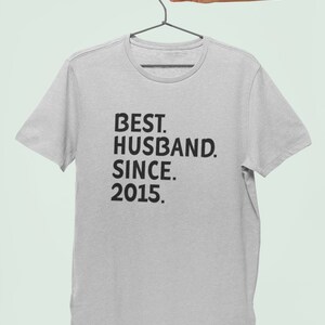 Op de afbeelding: Een grijs T-shirt met zwarte tekst die "BEST. HUSBAND. SINCE. 2015." luidt.