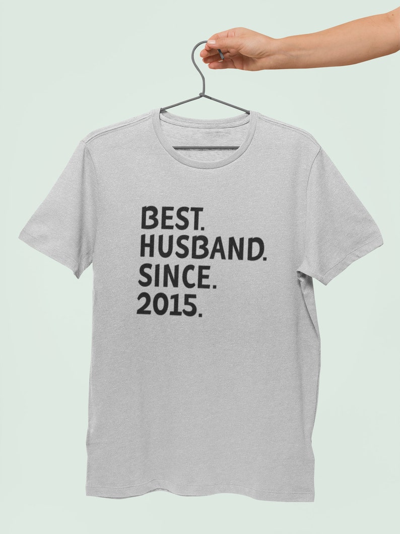 Op de afbeelding: Een grijs T-shirt met zwarte tekst die "BEST. HUSBAND. SINCE. 2015." luidt.