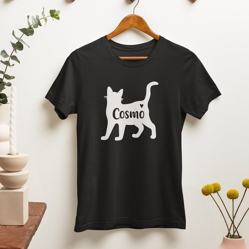 May include: Black t-shirt with a white silhouette of a cat and the name "Cosmo" printed on the front.