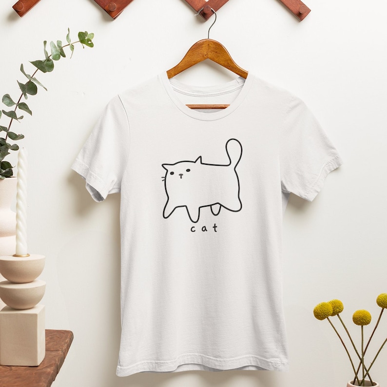 May include: White t-shirt with a simple black line drawing of a cat and the word "cat" underneath.