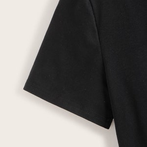 May include: Close-up of the black short sleeve of a t-shirt. The sleeve has a stitched hem.