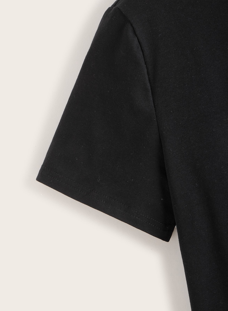 May include: Close-up of the black short sleeve of a t-shirt. The sleeve has a stitched hem.