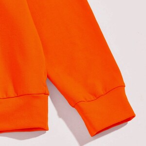 May include: Close-up of the orange fabric cuff of a long-sleeved sweatshirt.