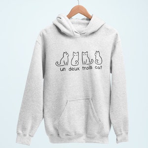 Op de afbeelding: Een grijs hoodie met een zwarte afbeelding van drie katten en de tekst "un deux trois cat".