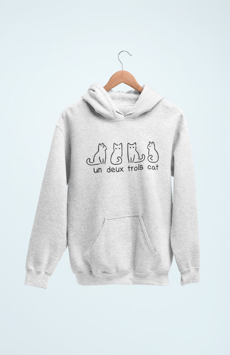 Op de afbeelding: Een grijs hoodie met een zwarte afbeelding van drie katten en de tekst "un deux trois cat".