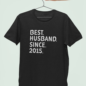 Op de afbeelding: Zwart T-shirt met witte tekst die "BEST. HUSBAND. SINCE. 2015." luidt.