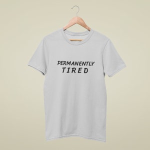 May include: A light gray t-shirt with the text "PERMANENTLY TIRED" printed in black.