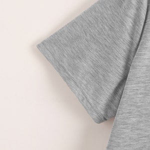May include: Close-up of the sleeve of a gray t-shirt. The fabric has a subtle texture.
