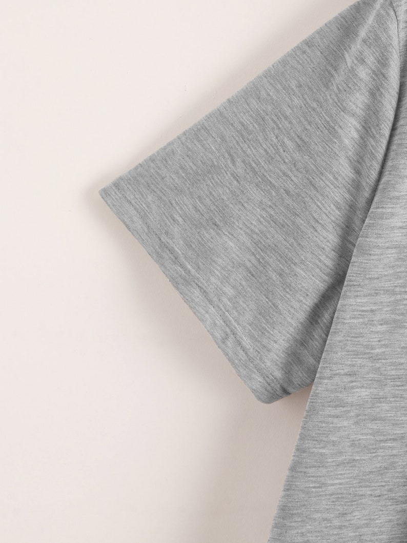 May include: Close-up of the sleeve of a gray t-shirt. The fabric has a subtle texture.