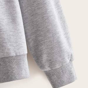 May include: Gray sweatshirt with long sleeves and ribbed cuffs. The sweatshirt is made of a soft, comfortable fabric.