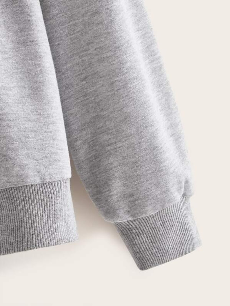 May include: Gray sweatshirt with long sleeves and ribbed cuffs. The sweatshirt is made of a soft, comfortable fabric.