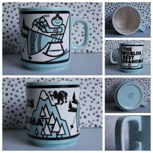 May include: A light blue ceramic mug with a black and white design of a woman sitting in a rocking chair. The mug has a handle and says "The World's Best Grandma" on the front.