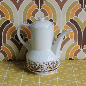 May include: White ceramic coffee pot with a brown, yellow and black geometric design. The pot has a lid and a spout.