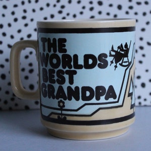 May include: A beige ceramic mug with a blue and brown design. The mug has a handle and says "The Worlds Best Grandpa" in black letters.