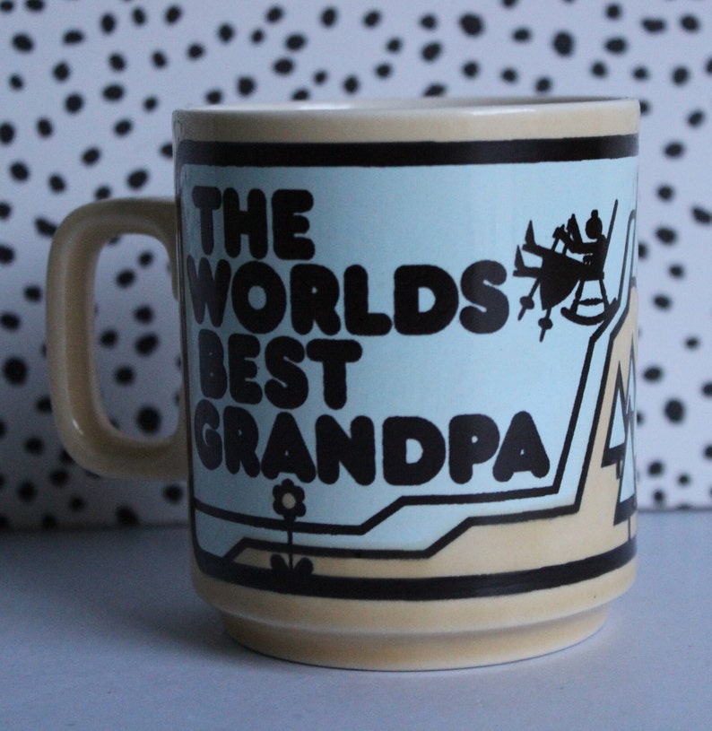 May include: A beige ceramic mug with a blue and brown design. The mug has a handle and says "The Worlds Best Grandpa" in black letters.
