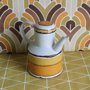 May include: A retro ceramic teapot with a white body, a curved handle, and a spout. The teapot has horizontal bands of yellow and orange, with brown trim. The lid is white with a yellow and brown design.