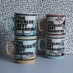 May include: Four ceramic mugs with colourful designs and the text "The Worlds Best" followed by "Grandma", "Grandpa", "Daughter", and "Husband".