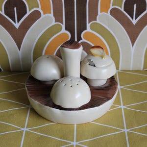 May include: A ceramic mushroom-shaped salt and pepper set with a matching sugar bowl. The set features a brown and cream colour scheme, with the mushroom caps and base in cream and the stems and underside in brown.
