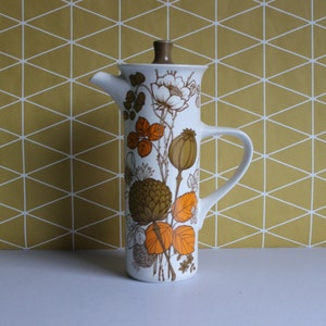 May include: A white ceramic coffee pot with a brown lid and handle. The pot features a floral design in brown and orange. The design includes flowers, leaves, and seed pods. The pot is tall and slender, with a spout for pouring.
