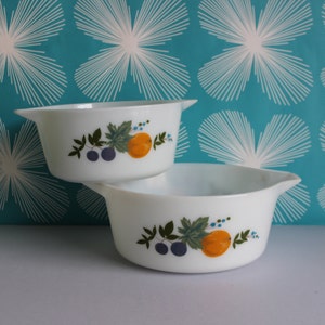 May include: Two white ceramic baking dishes with a fruit design. The design features a green leaf, orange fruit, and blue berries.