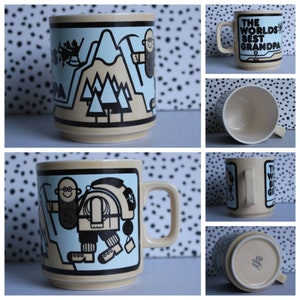 May include: A beige ceramic mug featuring a black and white illustration of a man with a beard and a backpack hiking up a mountain. The mug has a blue background and the text "The World's Best Grandpa" is printed on the side.
