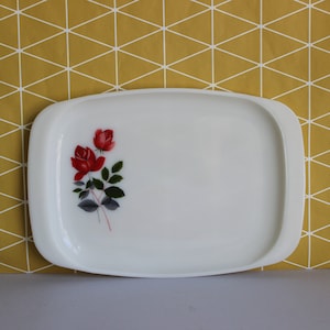 May include: A white rectangular serving tray with rounded edges. The tray features a floral design of red roses with green leaves on a gray stem. The background is a yellow geometric pattern.