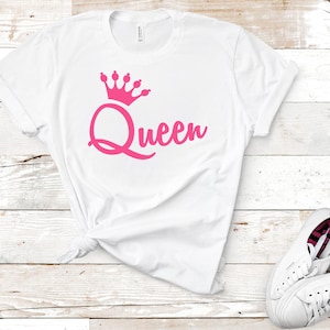 May include: White t-shirt with a pink crown and the word "Queen" in a pink cursive font.