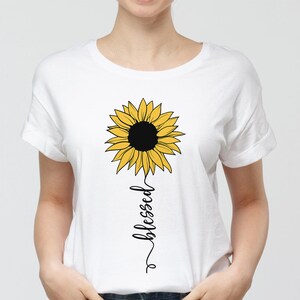 May include: White t-shirt with a yellow sunflower graphic and the word "blessed" written vertically below it.