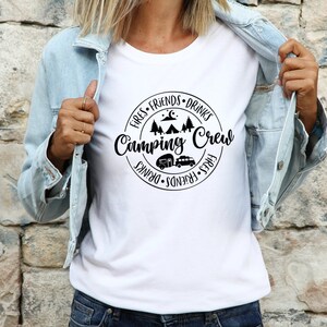 K&ouml;nnte beinhalten: Wei&szlig;es T-Shirt mit einem schwarzen Kreis-Motiv, auf dem "Fires, Friends, Drinks, Camping Crew, Drinks, Friends, Fires" steht. Das Motiv enth&auml;lt auch ein Lagerfeuer, ein Zelt und zwei Wohnmobile.