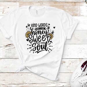 May include: White t-shirt with a black and yellow graphic design that says "Kind words are like honey sweet to the soul".
