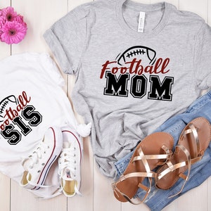 May include: A grey t-shirt with the text Football MOM and a football graphic, a white t-shirt with the text Football SIS and a football graphic, blue denim jeans, a pair of white canvas sneakers, and a pair of metallic gold strappy sandals.